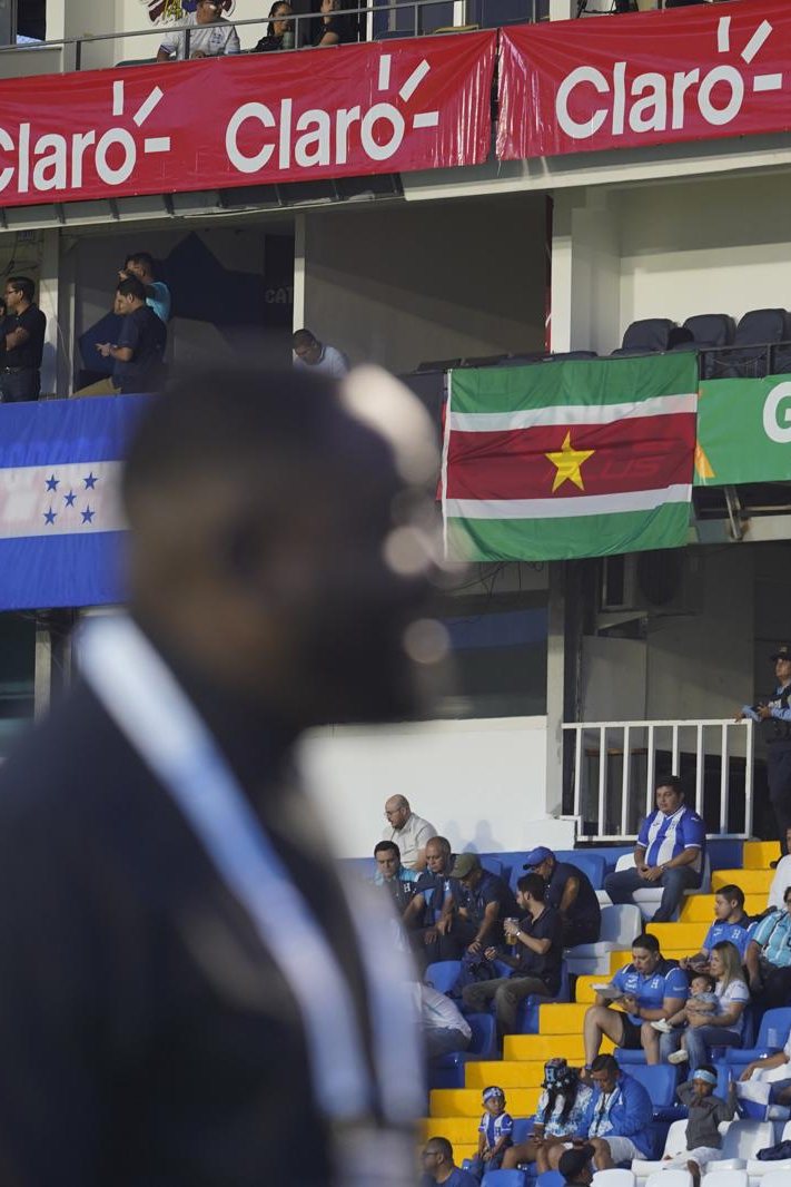 Brian Tevreden langs het veld, op de tribune hangt de Surinaamse vlag